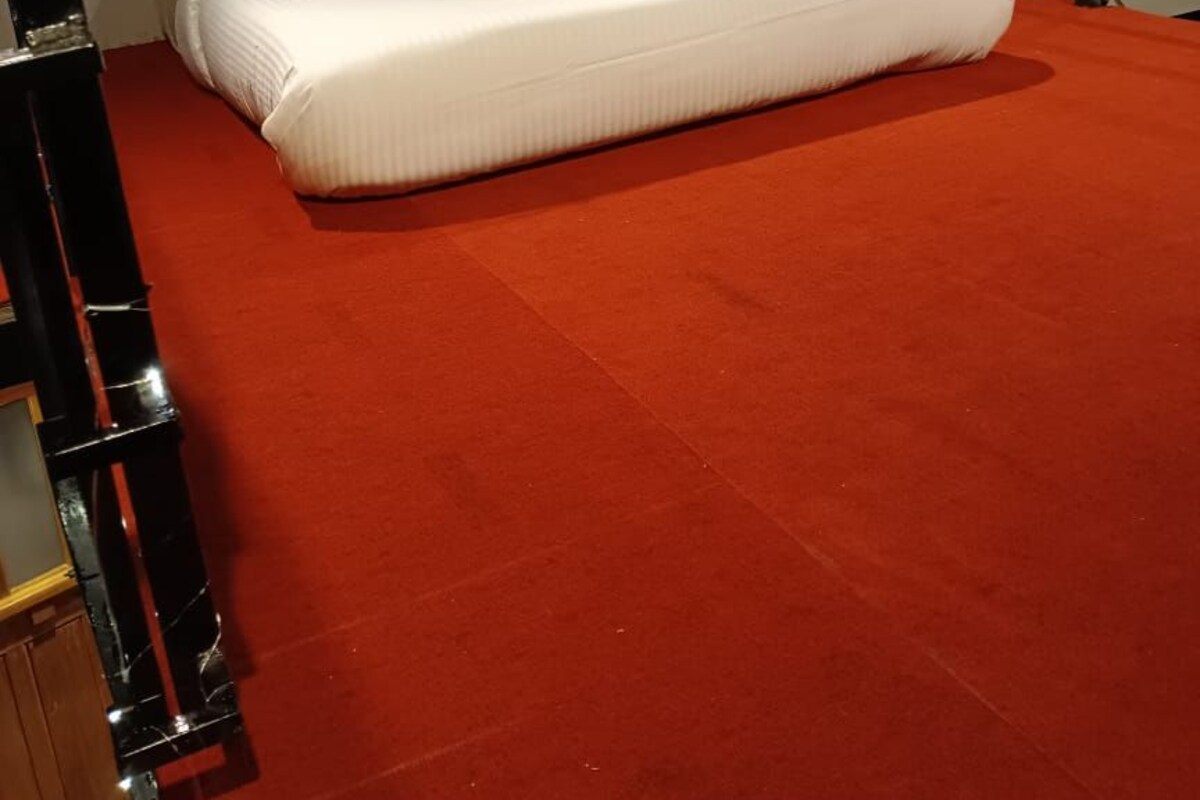 A single bed with white bedding in a room with a red carpet and a wooden ceiling.