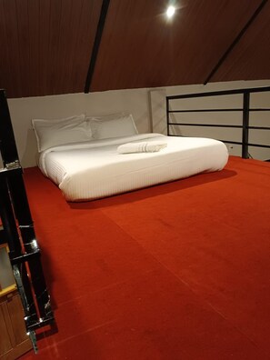 A single bed with white bedding in a room with a red carpet and a wooden ceiling. - The Frame Resorts Ooty (Coonoor)