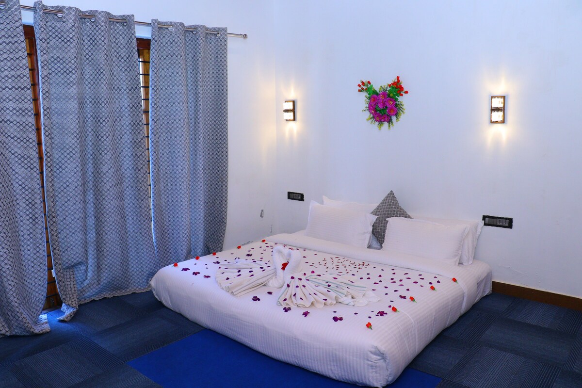 A hotel room with a bed, curtains, wall-mounted lights, and a flower arrangement.