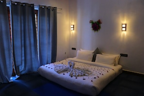 A hotel room with a neatly made bed, a wall-mounted light fixture, and a decorative wall hanging. - The Frame Resorts Ooty (Coonoor)