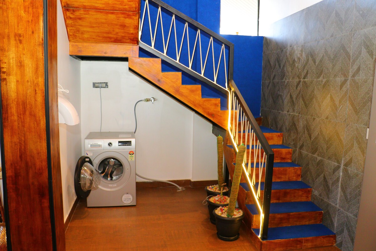 A laundry area with a washing machine, a staircase with blue steps, and a wall with a geometric pattern.