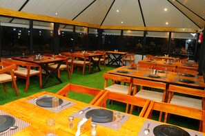 A restaurant with multiple tables and chairs, arranged in a tent-like structure with a green carpet. - The Frame Resorts Ooty (Coonoor)