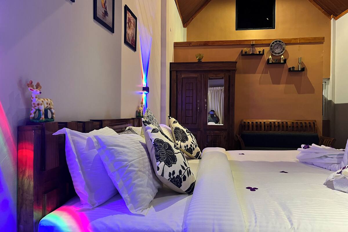 A hotel room with a bed, a wooden headboard, a nightstand, a mirror, a clock, and a window with curtains.