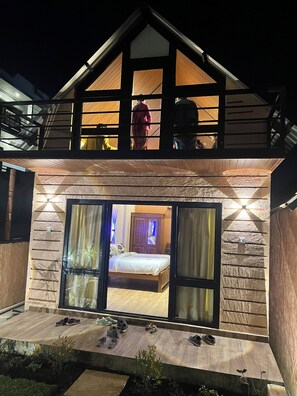 A two-story house with a balcony, a bedroom with a bed and curtains, and a sliding glass door. - The Frame Resorts Ooty (Coonoor)