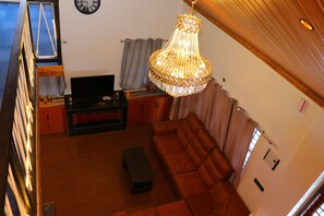 A living room with a sofa, a television, a chandelier, and a staircase. - The Frame Resorts Ooty (Coonoor)