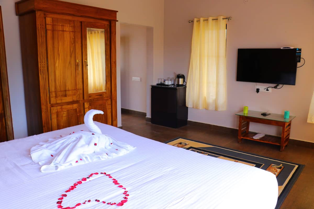 A hotel room with a bed, a wooden wardrobe, a television, a small table, and a curtain.