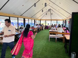 A tented dining area with tables and chairs, a person in traditional attire, and a man holding a plate. - The Frame Resorts Ooty (Coonoor)