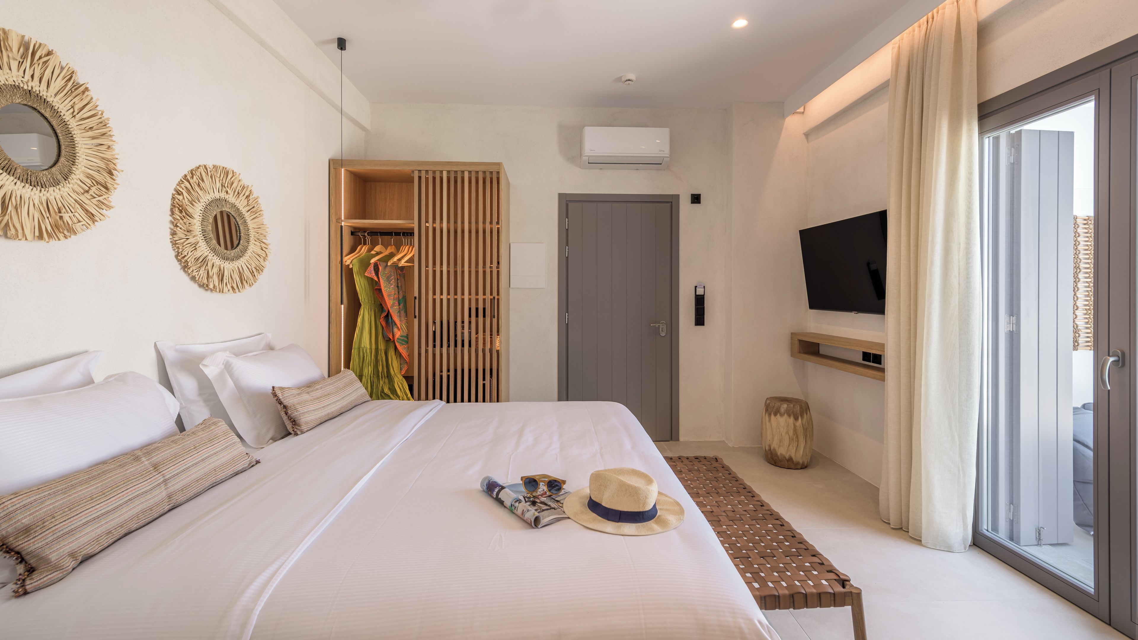 A modern hotel room with a large bed, a television mounted on the wall, and a sliding glass door leading to a balcony.