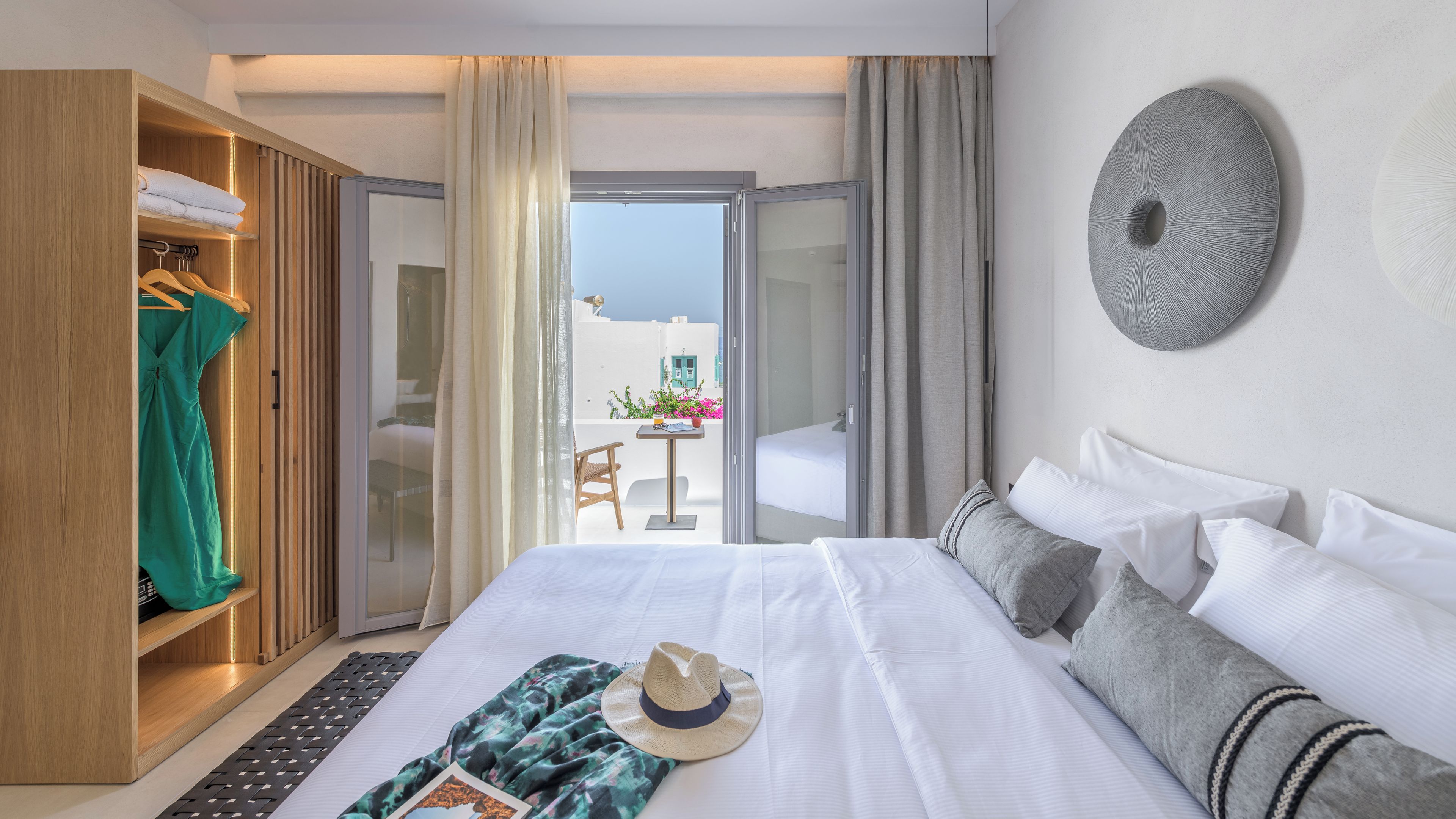 A hotel room with a bed, a wardrobe, a balcony with a view, and a round wall decoration.