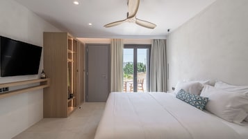 Una habitación de hotel moderna con una cama grande, un televisor montado en la pared, un armario y un balcón con mobiliario exterior.