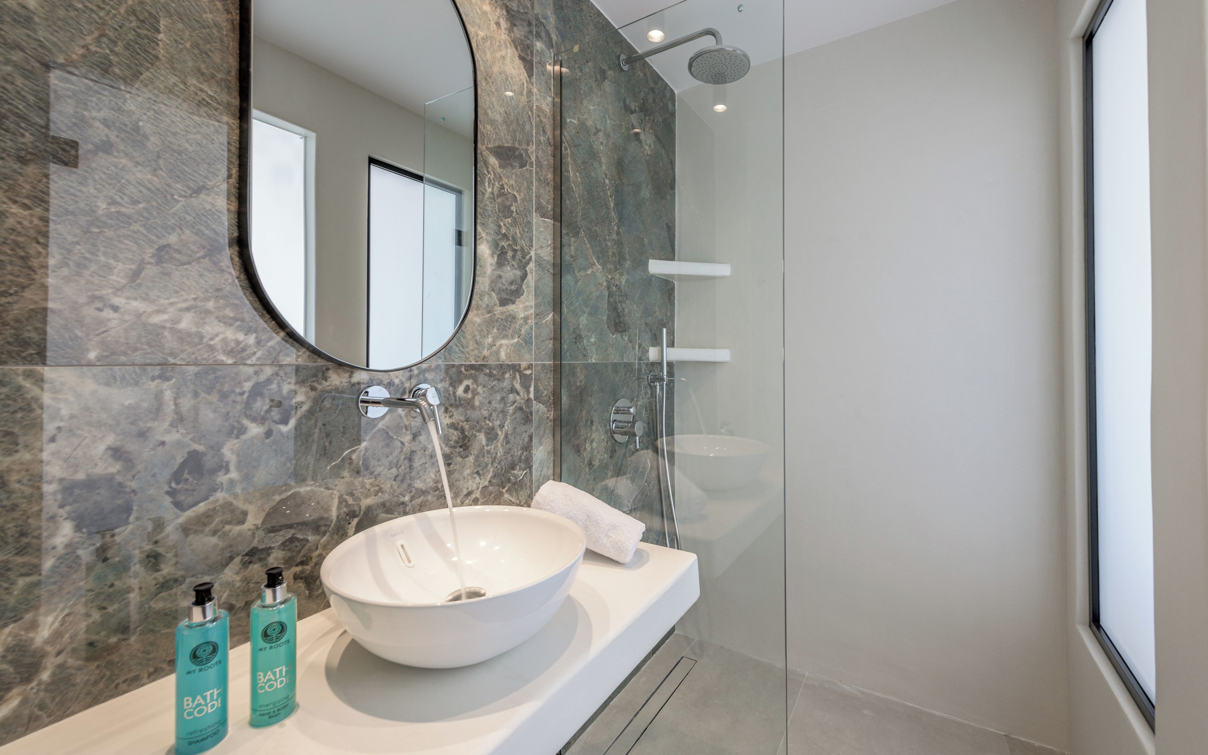 A modern bathroom with a large oval sink, a glass shower enclosure, and a mirror above the sink.
