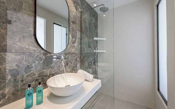 A modern bathroom with a large oval sink, a glass shower enclosure, and a mirror above the sink. - Nove Milos Luxury (Milos)