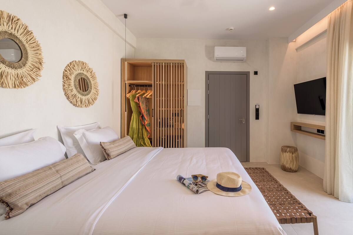 A modern hotel room with a large bed, a television mounted on the wall, and a sliding glass door leading to a balcony.
