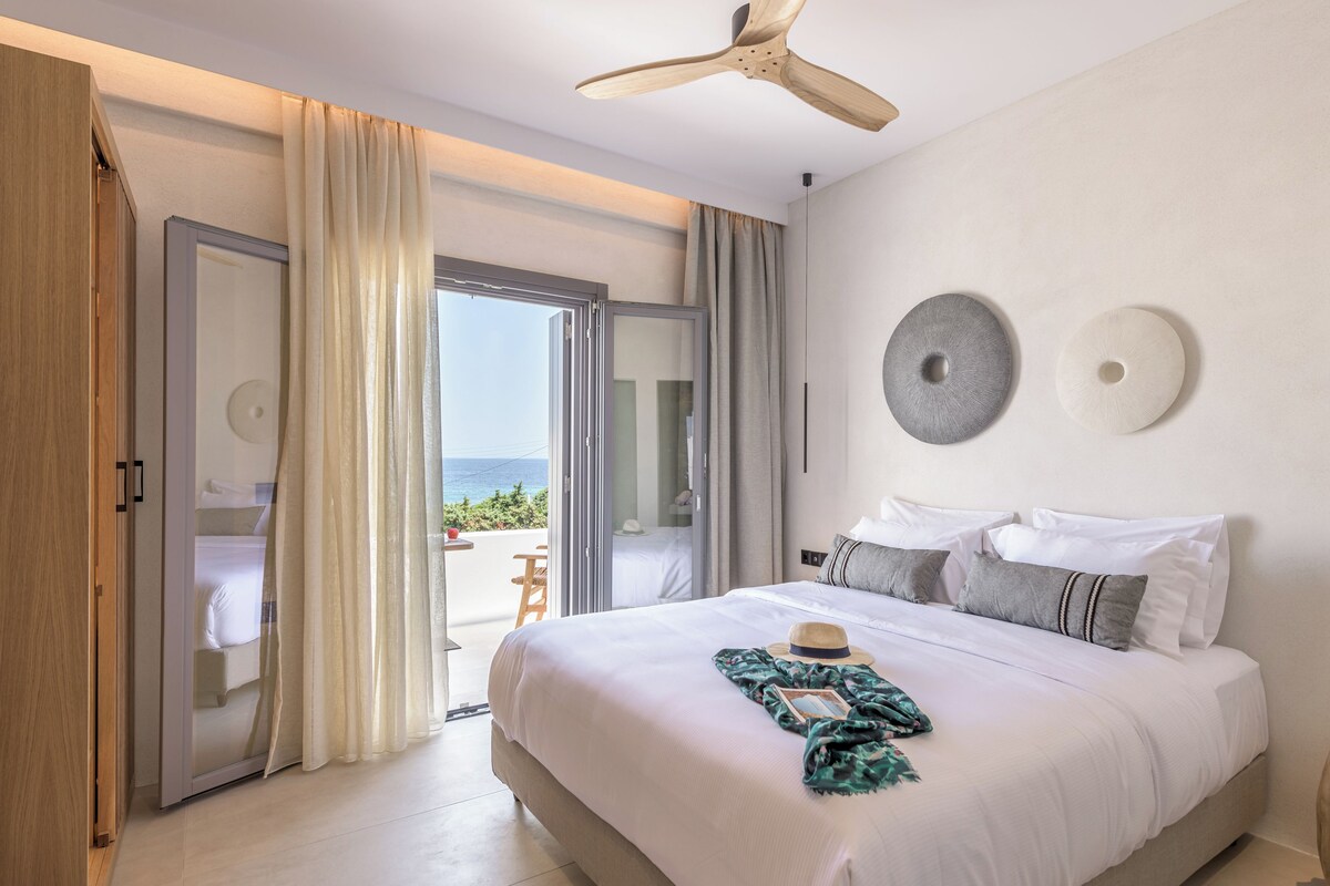 Ein Schlafzimmer mit einem großen Bett, einem Deckenventilator und Meerblick durch eine Schiebetür.