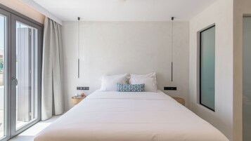 Quarto de hotel moderno com uma cama grande, vista pela porta de vidro e uma janela ampla à direita.