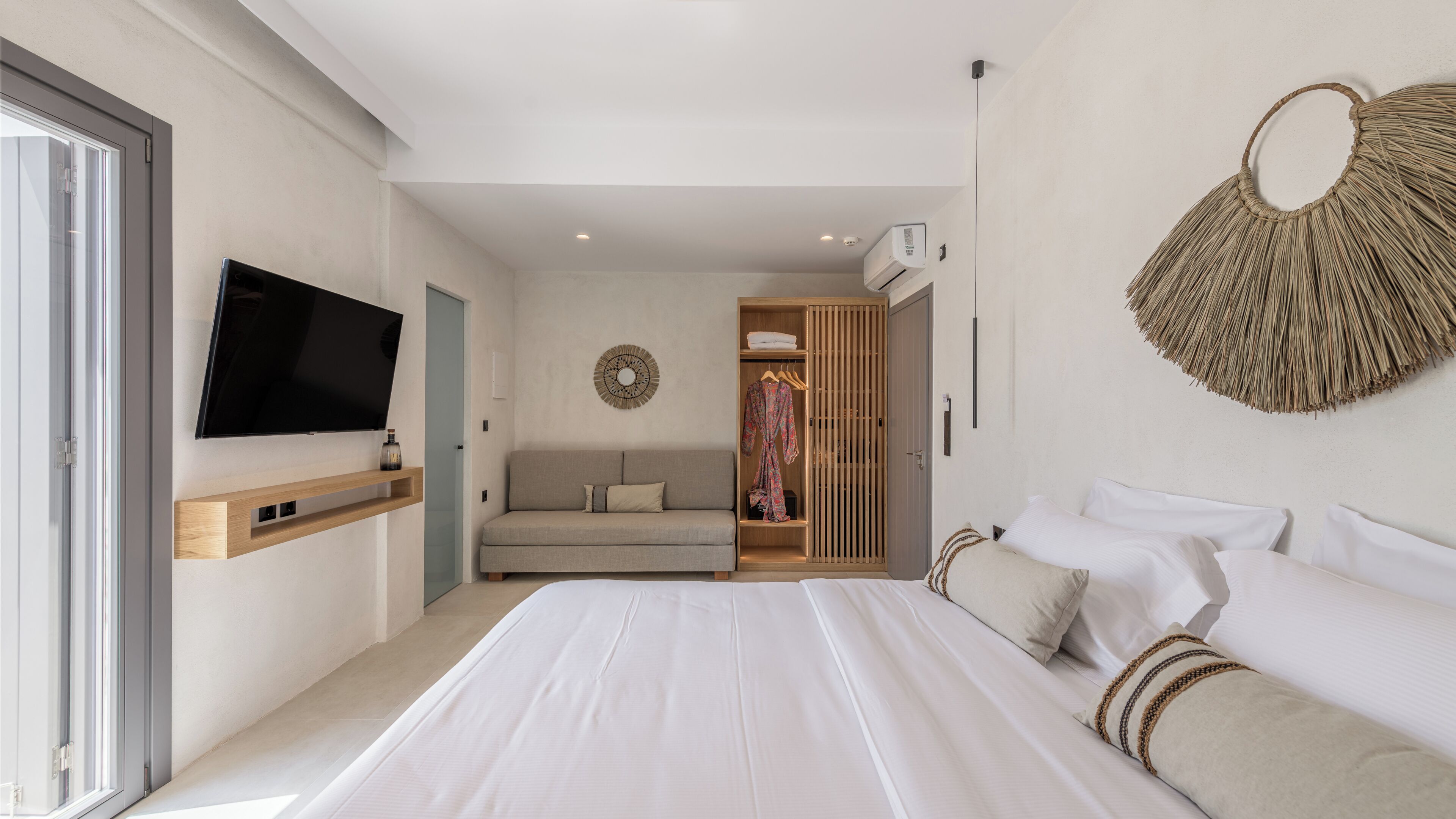 A modern hotel room with a large bed, a sofa, a wardrobe, and a television.