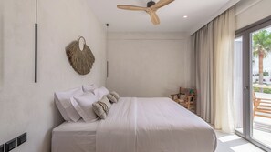 A bedroom with a bed, a ceiling fan, a wall-mounted macrame piece, and a view of the outdoors through a large window. - Nove Milos Luxury (Milos)