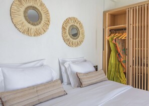 A hotel room with a bed, two wall mirrors, and a wooden wardrobe with hanging clothes. - Nove Milos Luxury (Milos)