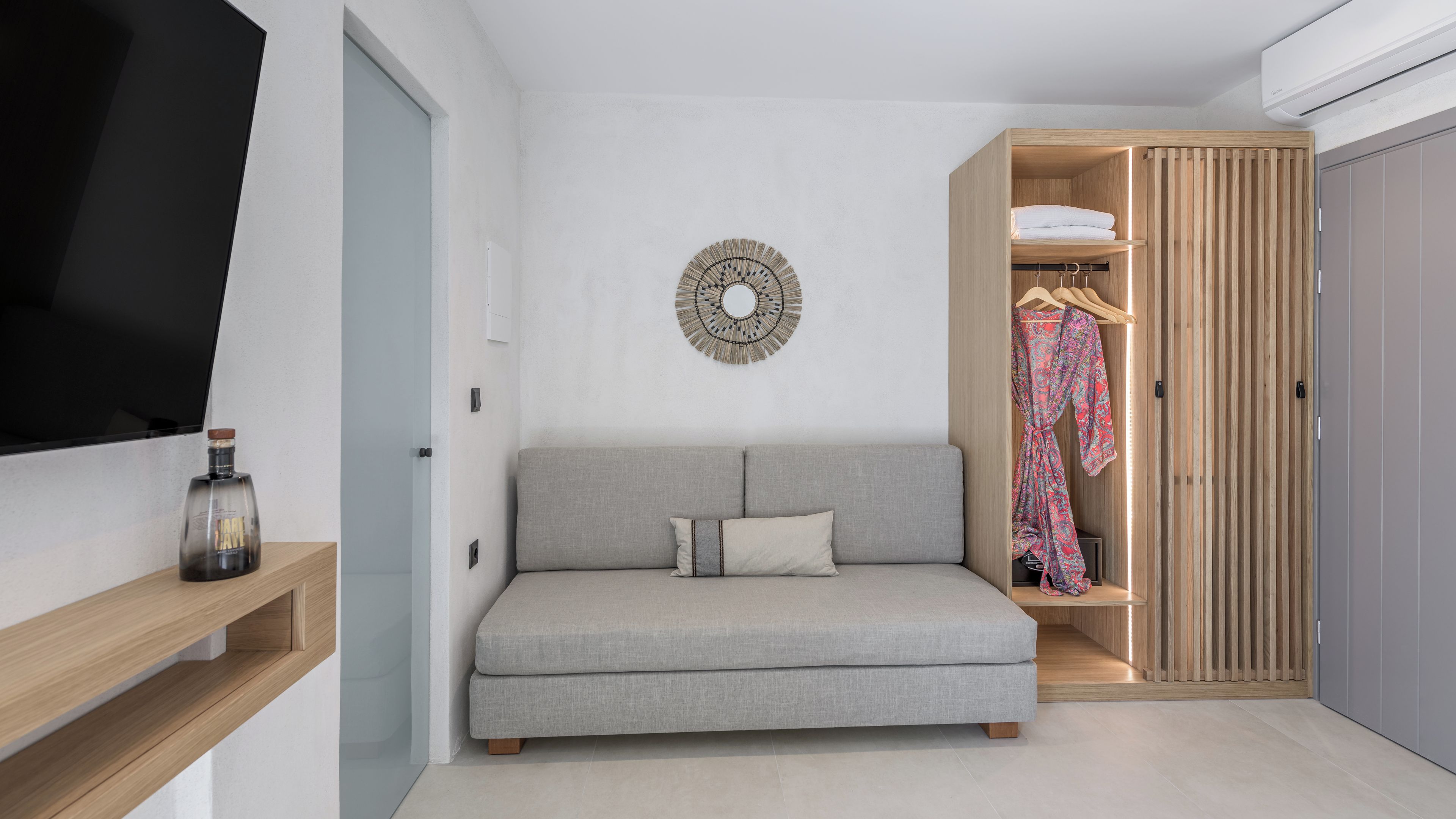 Um espaço de estar moderno e compacto, com um sofá cinzento, um guarda-roupa de madeira e um objeto decorativo fixado na parede.