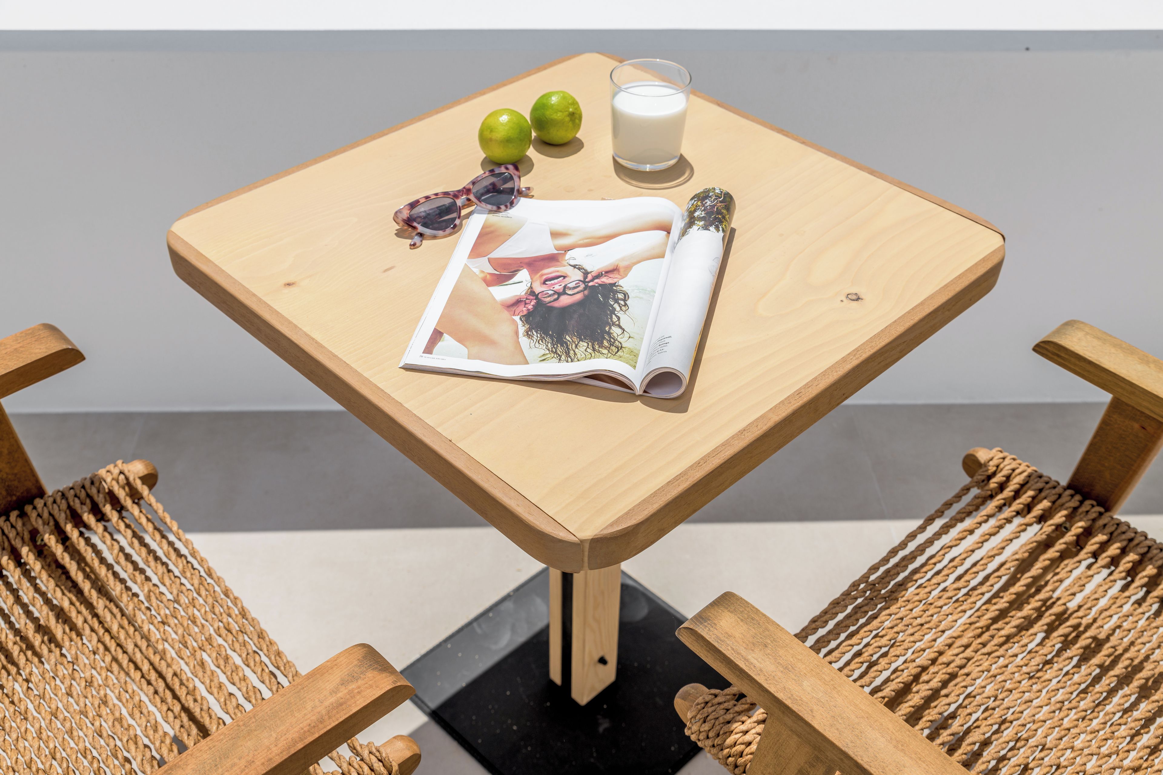 A wooden table with a magazine, two green apples, a glass of milk, and sunglasses.