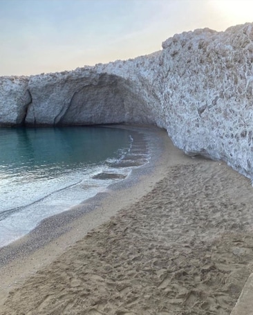 A beach with a rocky cliff and calm water.