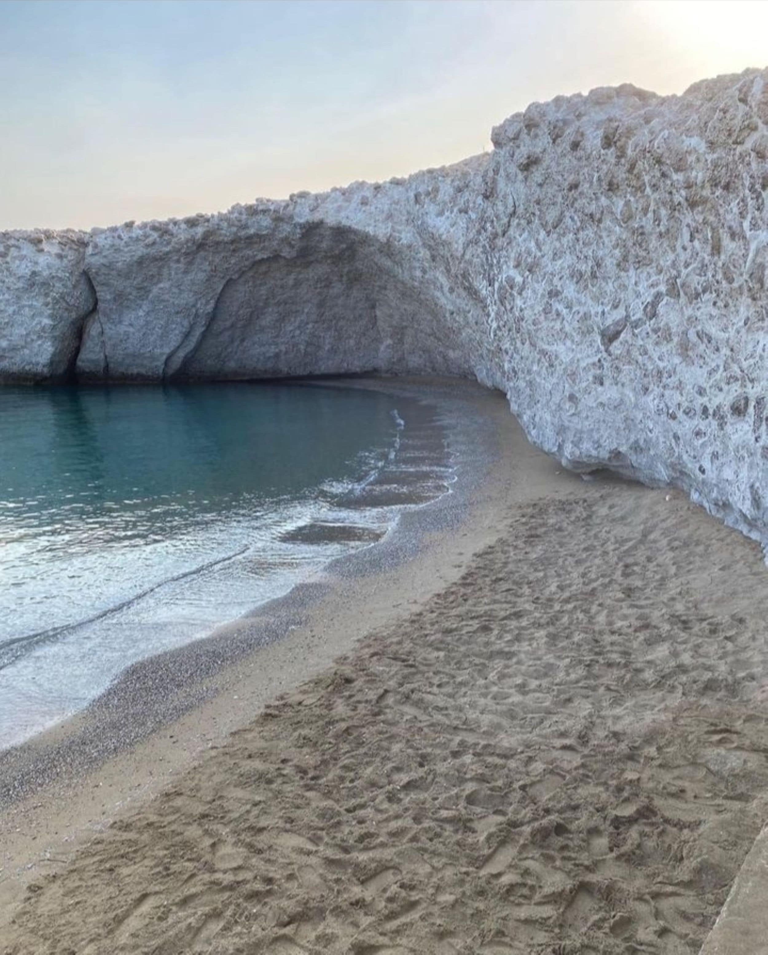 A beach with a rocky cliff and calm water.