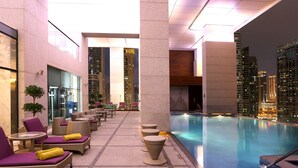 Una piscina interior con sillas de descanso y mesas, rodeada de edificios altos.
