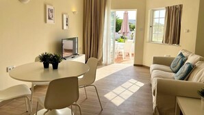 A modern living room with a round table, two chairs, a sofa, and a TV. There is a sliding glass door leading to an outdoor area with a patio table and chairs. - Balaia Plaza Al (Albufeira)