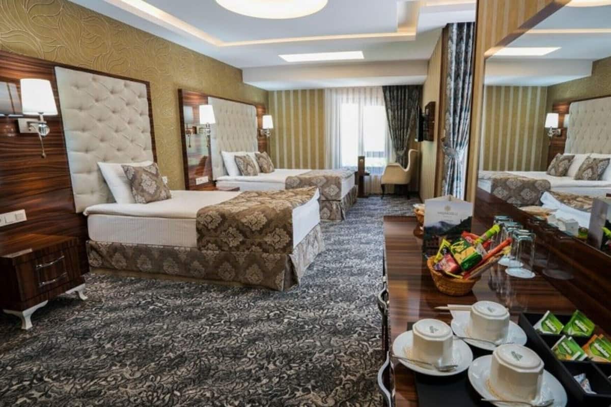 A hotel room with two beds, a large mirror, a vanity with a mirror, a small table with a basket of toiletries, and a view of the city.