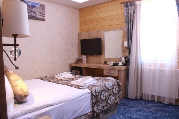 Une chambre d’hôtel équipée d’un lit, d’un bureau, d’un téléviseur à écran plat, d’un miroir, d’une lampe et d’une fenêtre avec des rideaux.
