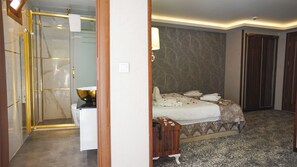 A hotel room with a glass shower enclosure, a bedside table with a bowl, a bed with a patterned bedspread, and a wooden nightstand. - Ayder Hasimoglu Otel - Eur (Çamlıhemşin)