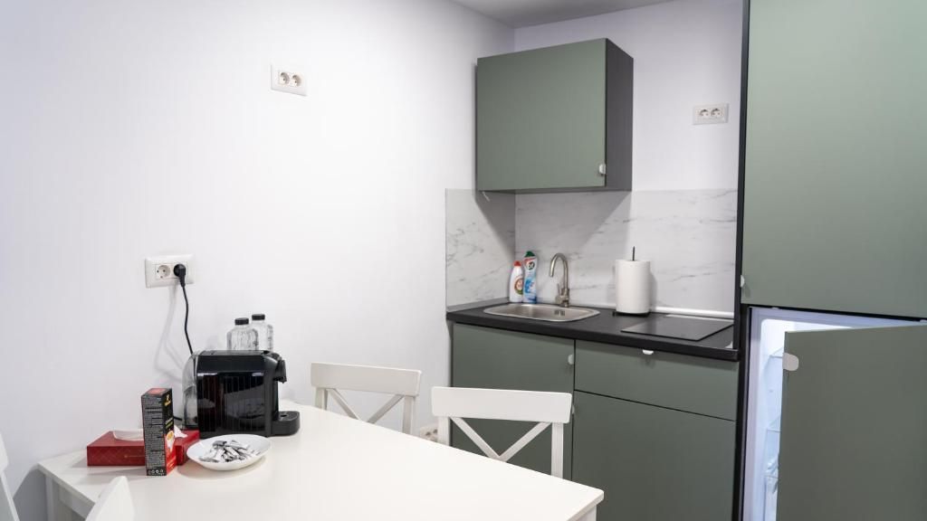 A compact kitchen with a white table, two white chairs, a black coffee maker, a sink, and a green cabinet.