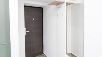 Un pasillo con una puerta oscura, paredes blancas y suelo de baldosas.