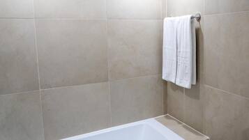 A bathroom with beige tiles, a white bathtub, and a towel hanging on a metal rack.