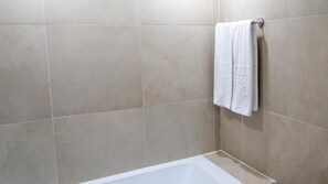 Une salle de bain avec des carreaux de couleur beige, une baignoire blanche et une serviette suspendue à un porte-serviettes en métal.