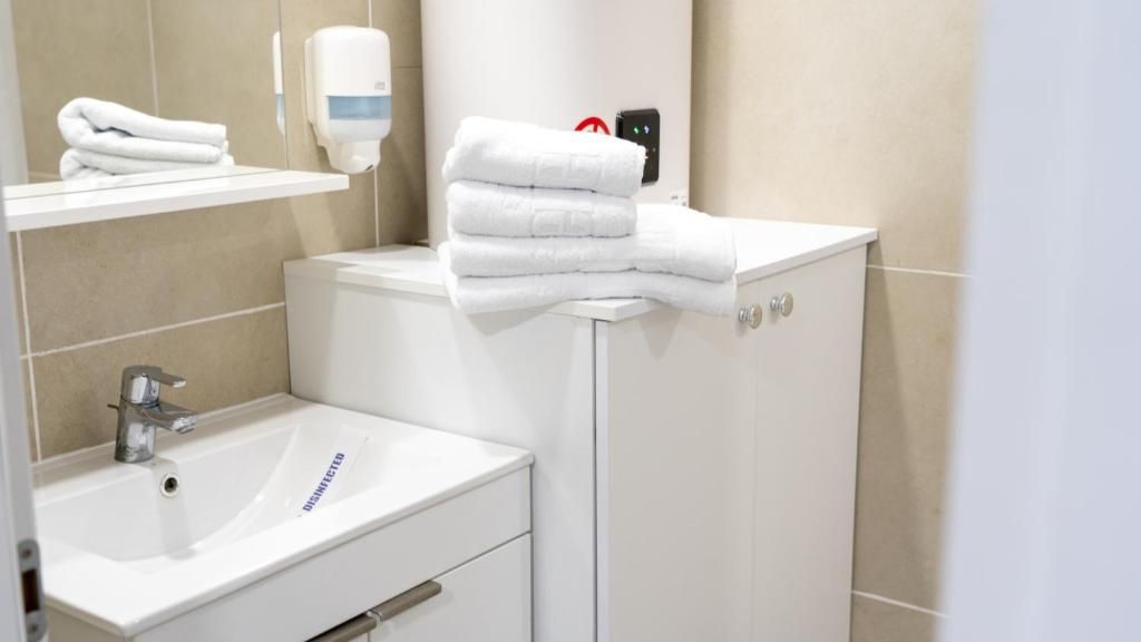 A bathroom with a sink, a mirror, a towel dispenser, and a stack of towels on a cabinet.