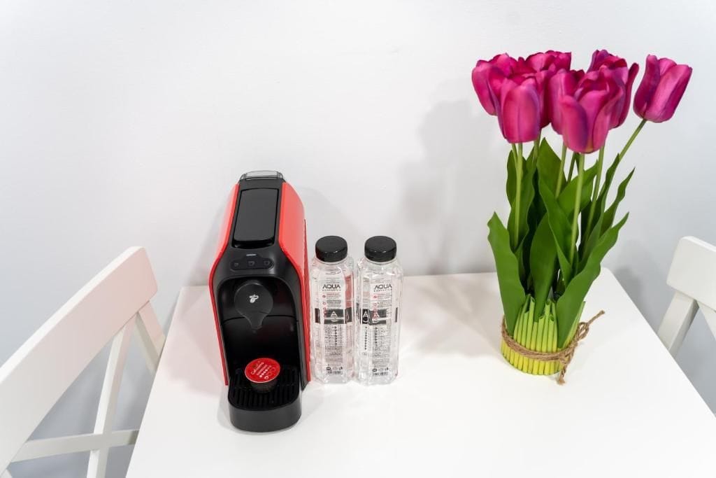 Een rode en zwarte waterfilter, twee heldere waterflessen, en een vaas met roze tulpen op een witte tafel.
