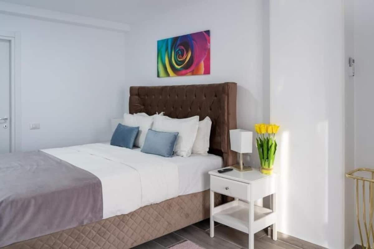 A bedroom with a bed, bedside table, lamp, and a vase of flowers.