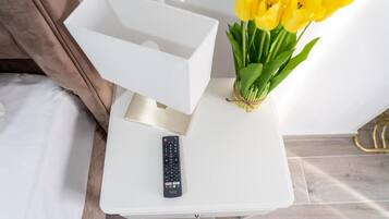 A white bedside table with a remote control and a bouquet of yellow tulips.