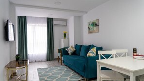 A modern living room with a teal sofa, a white dining table, and a glass coffee table.