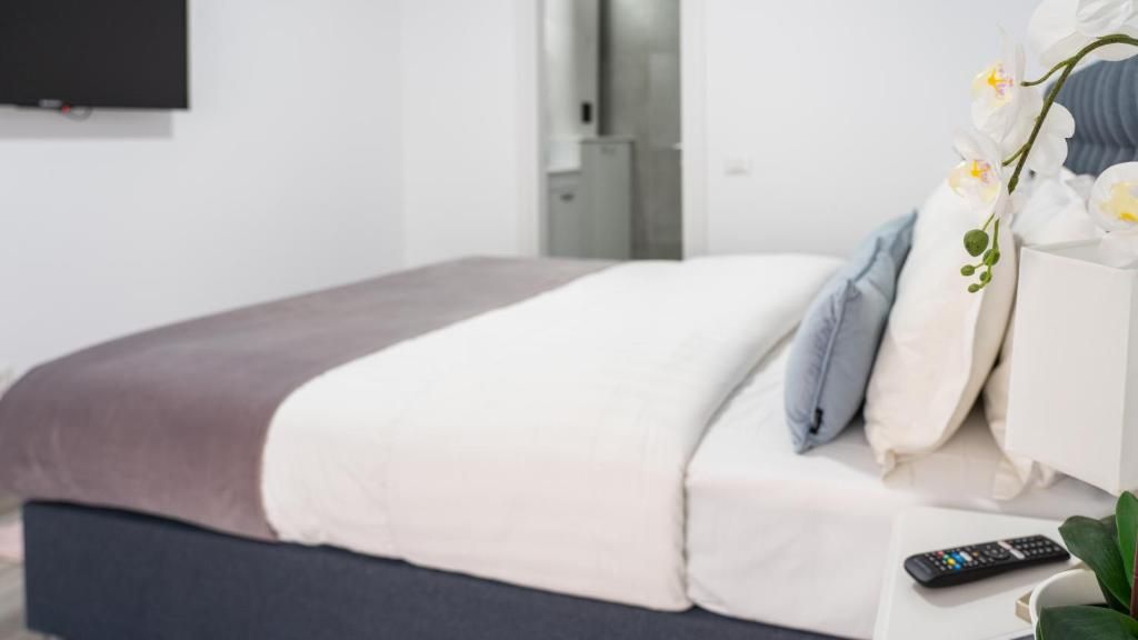 A neatly made bed with a brown headboard, a white pillow, and a remote control on a bedside table.