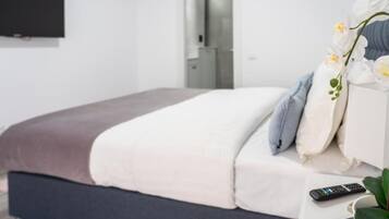 A neatly made bed with a brown headboard, a white pillow, and a remote control on a bedside table.