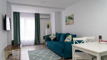 A modern living room with a teal sofa, a white dining table, and a glass coffee table.