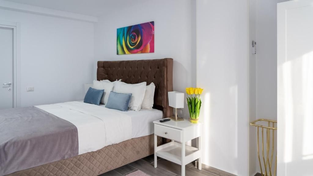 Un dormitorio con cama, mesita de noche, lámpara y un florero con flores.