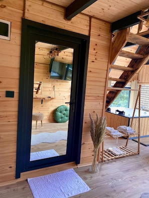 A wooden cabin interior with a large mirror, a green cushioned stool, a hanging plant, and a wooden ladder. - Berva Bungalow (Çamlıhemşin)