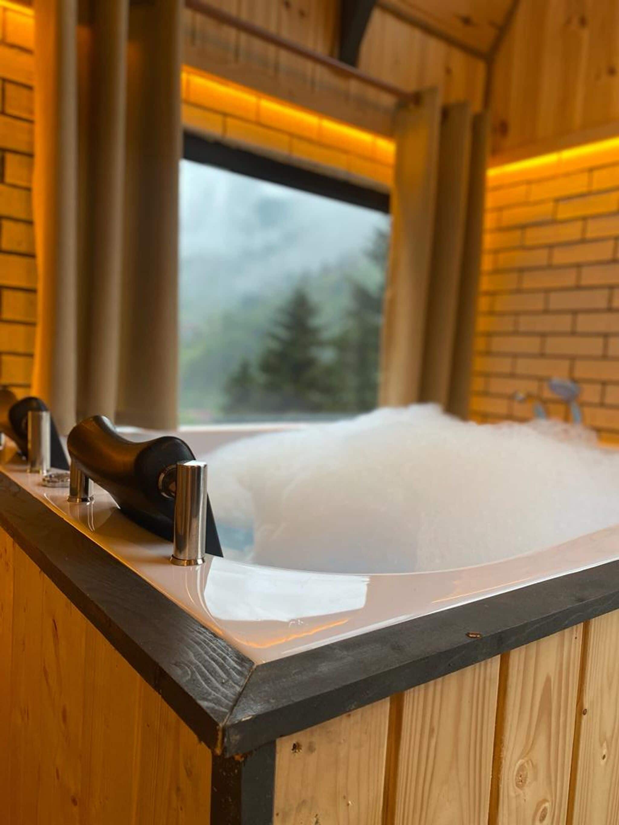 Eine Holzhütte mit einem großen Fenster, einer Badewanne und einer hölzernen Bank.