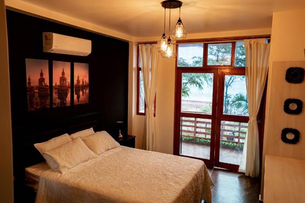 A bedroom with a bed, a window with curtains, a wall-mounted air conditioner, and a door leading outside.