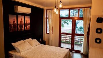 A bedroom with a bed, a window with curtains, a wall-mounted air conditioner, and a door leading outside.