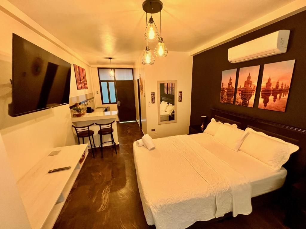 A hotel room with a large bed, a desk with chairs, a TV, and artwork on the walls.