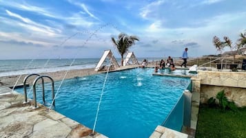 Una piscina con vista al océano, una palmera y una persona caminando.